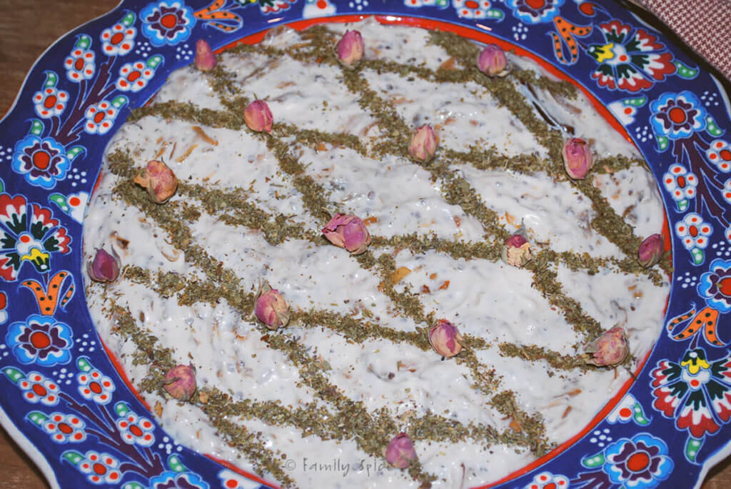 Closeup of a bowl of borani bademjan garnished with dried mint and rose petals