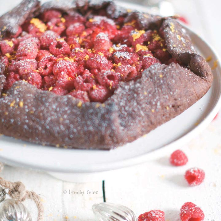 A baked chocolate raspberry galette on a white cake stand