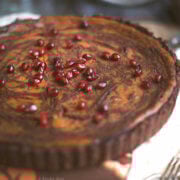Top view of a pumpkin pie with chocolate swirls baked in a chocolate pie shell topped with pomegranate arils