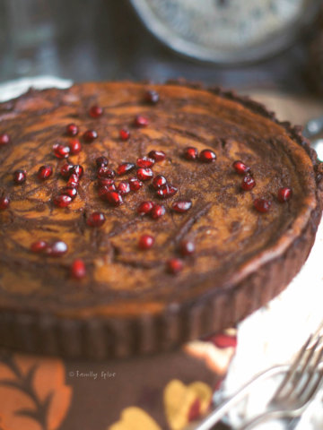 Top view of a pumpkin pie with chocolate swirls baked in a chocolate pie shell topped with pomegranate arils