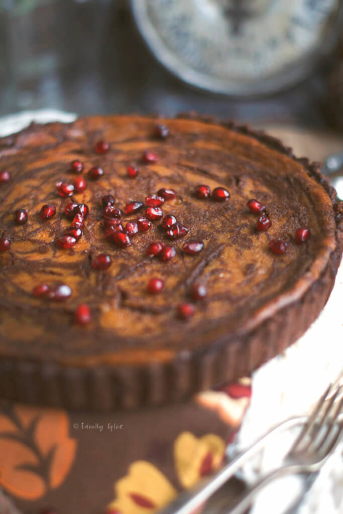 Top view of a pumpkin pie with chocolate swirls baked in a chocolate pie shell topped with pomegranate arils