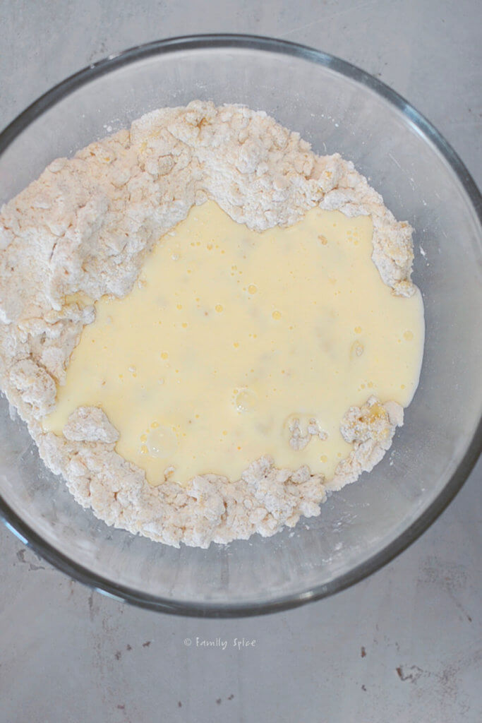 Adding yogurt mixture to flour mixture to make olive oil scone dough in a glass mixing bowl