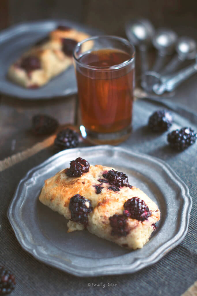 Closeup of a slice of blackberry scone on a pewter plate with a glass of tea