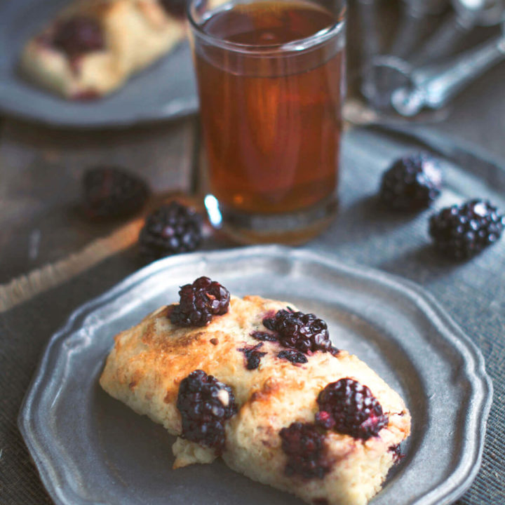 Closeup of a slice of blackberry scone on a pewter plate with a glass of tea