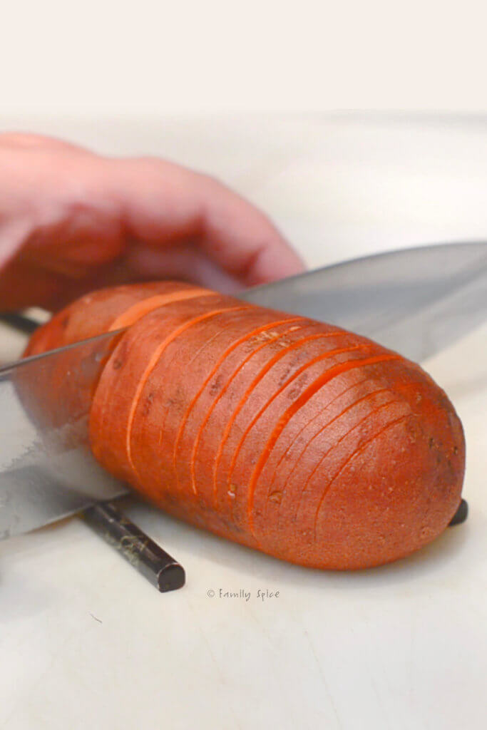 Cutting a hasselback sweet potato with chopsticks as guides