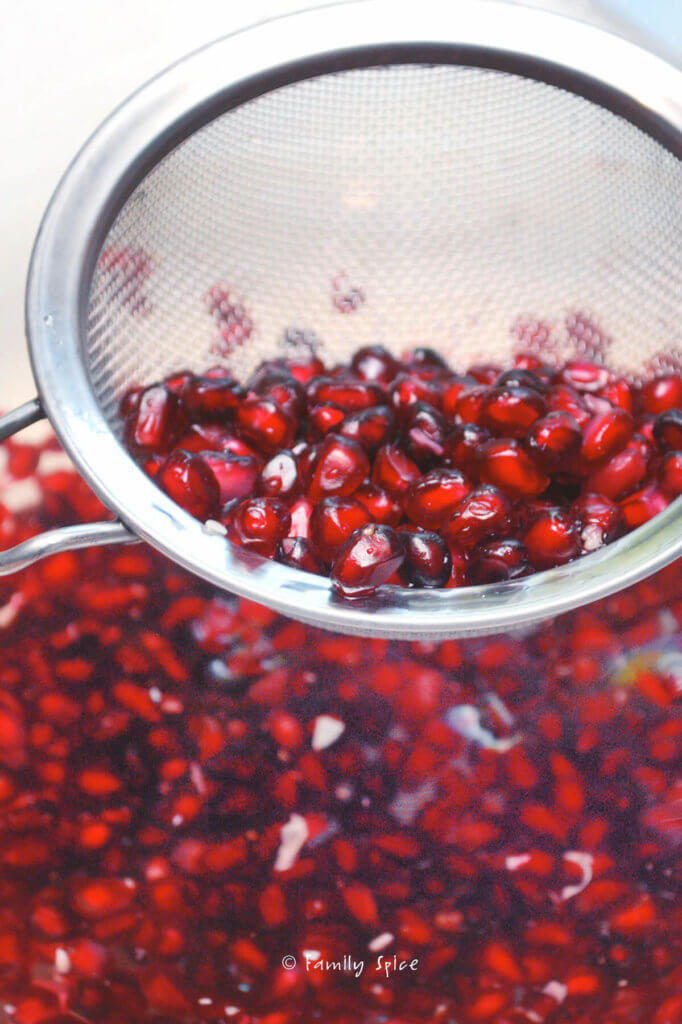 Straining pomegranate arils out of bowl filled with pomegranate and water