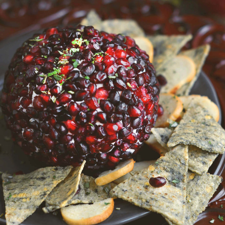 Close up of a pomegranate cheese ball with seedy chips on a rustic background
