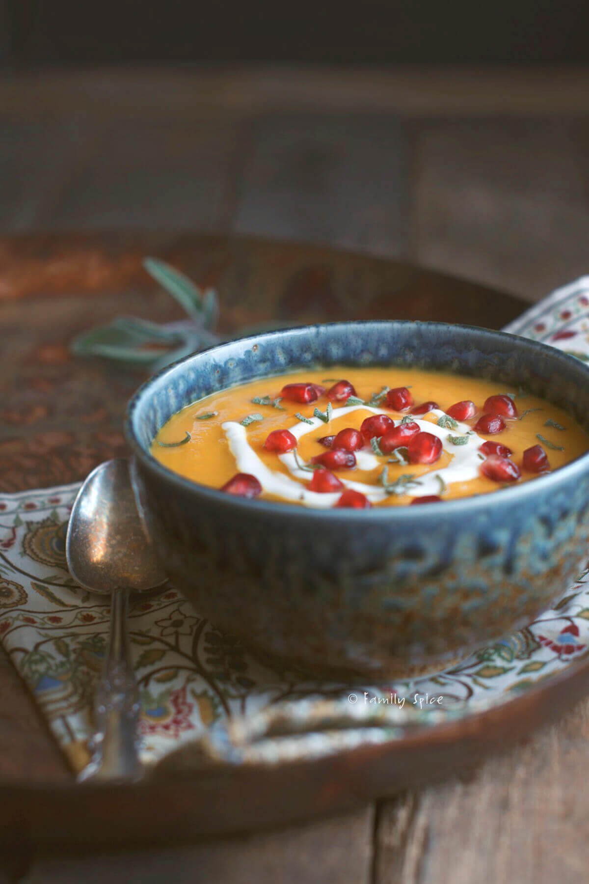 Side view of a bowl roasted acorn squash soup garnished with sage, pomegranate and sour cream