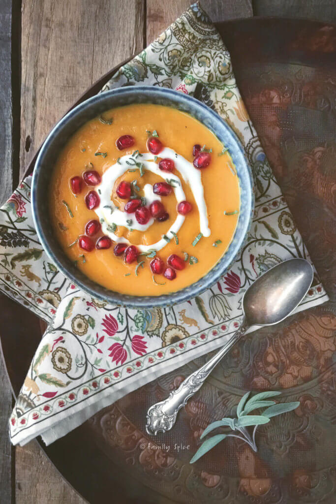 Top view of a bowl of roasted acorn squash soup garnished with sage, pomegranate and sour cream