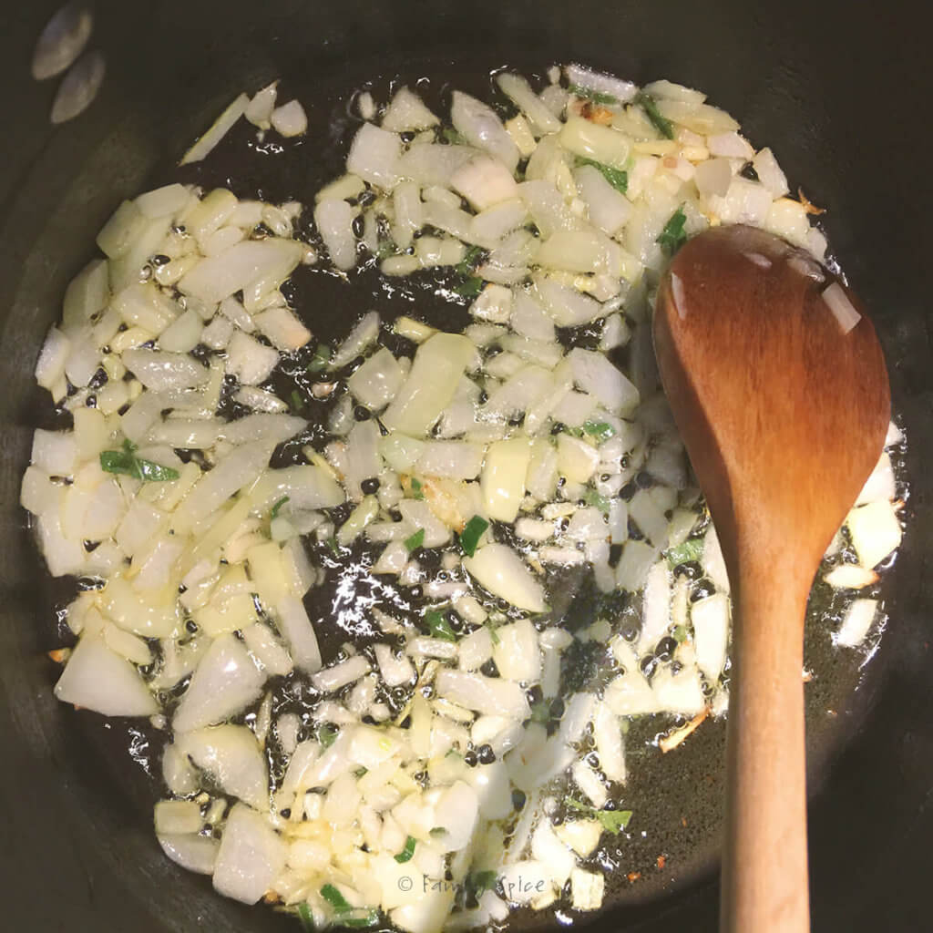 Pot with wooden spoon sautéing onions