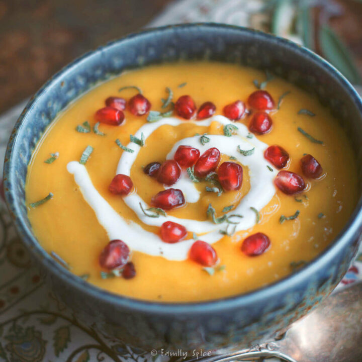 Closeup of a bowl of roasted acorn squash soup garnished with sage, pomegranate and sour cream