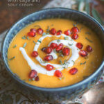 Closeup of a bowl of roasted acorn squash soup with sage and sour cream studded with pomegranate by FamilySpice.com