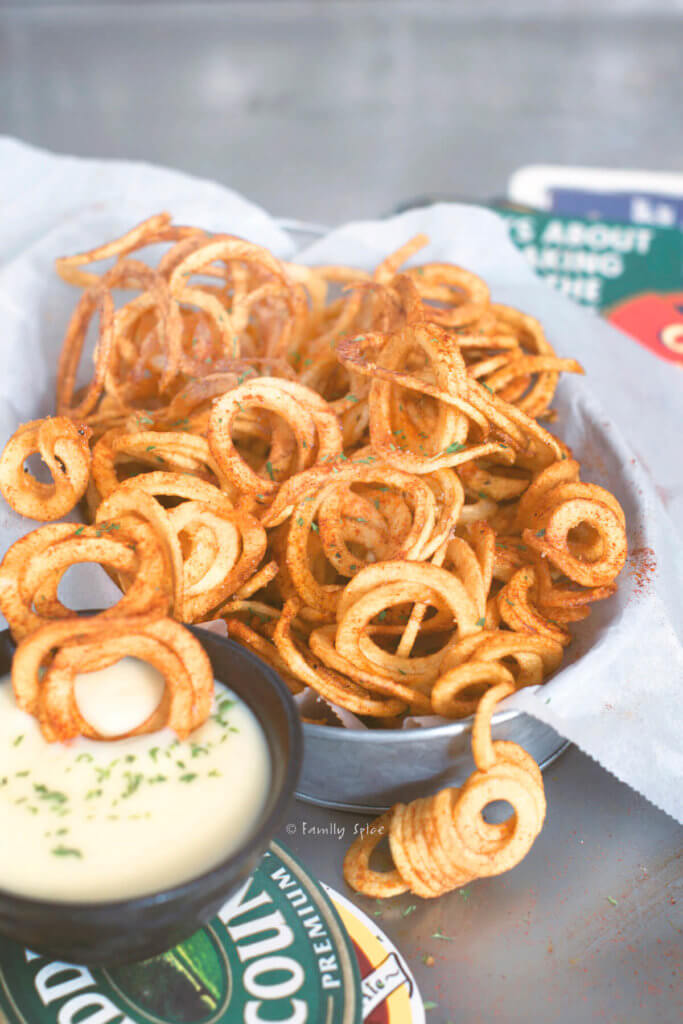 Closeup of a metal basket filled with curly fries with a small bowl of beer cheese dip next to it