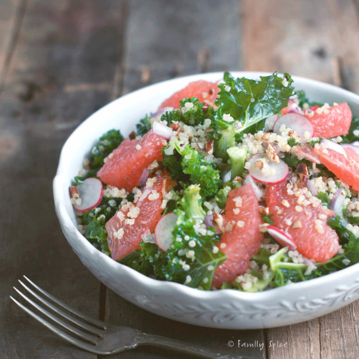 A white bowl with kale, grapefruit, quinoa salad on a rustic background