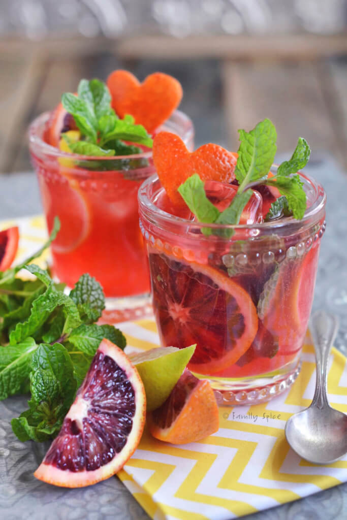 Close up of two glasses filled with blood orange mojito and garnished with blood oranges and mint