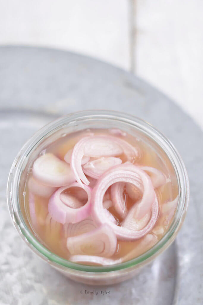 Sliced shallots covered in cider vinegar in a small glass jar