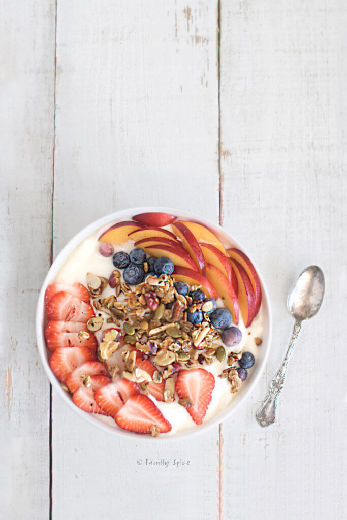 A bowl of yogurt with fruit and granola on a white background