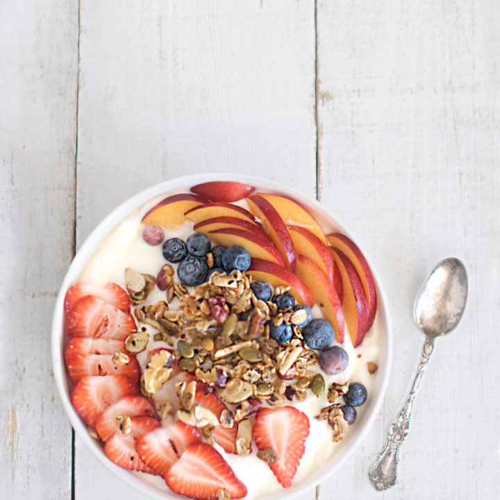 A bowl of yogurt with fruit and granola on a white background