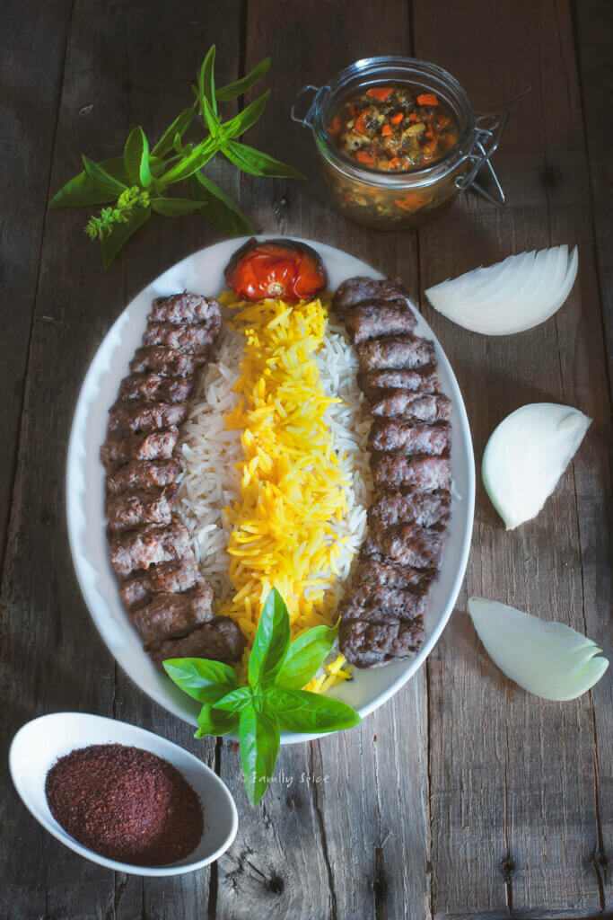 Top view of a plate with basmati rice with saffron and koobideh kabob with roast tomatoe, sumac, herbs and torshi