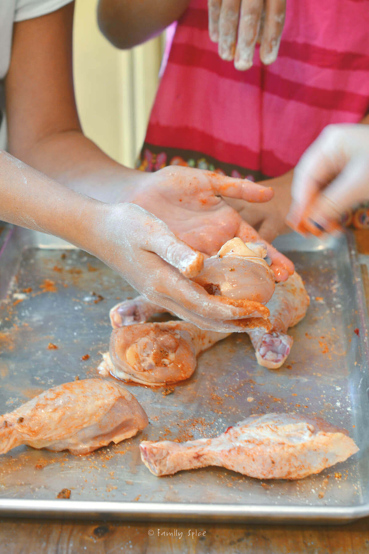 Kids seasoning chicken legs on a baking sheet