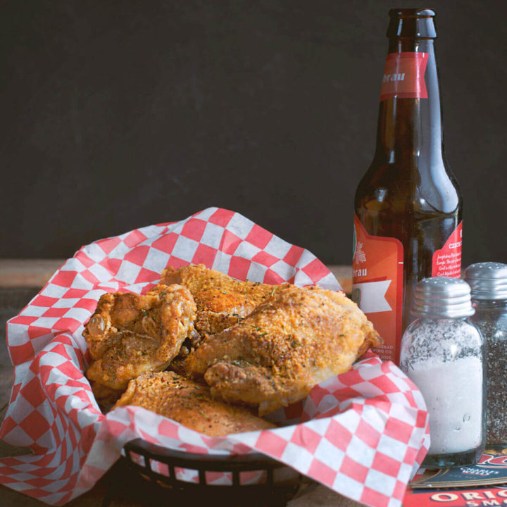 A paper lined basket with oven fried chicken pieces and a bottle of beer next to it