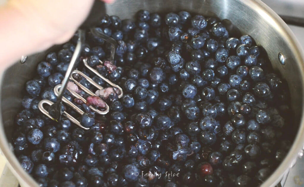 Making blueberry jam in a stainless pot and mashing it with a potato masher