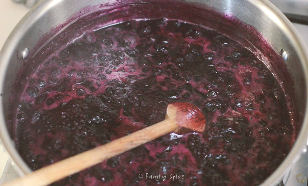 A wooden spoon stirring hot blueberry jam in a stainless pot