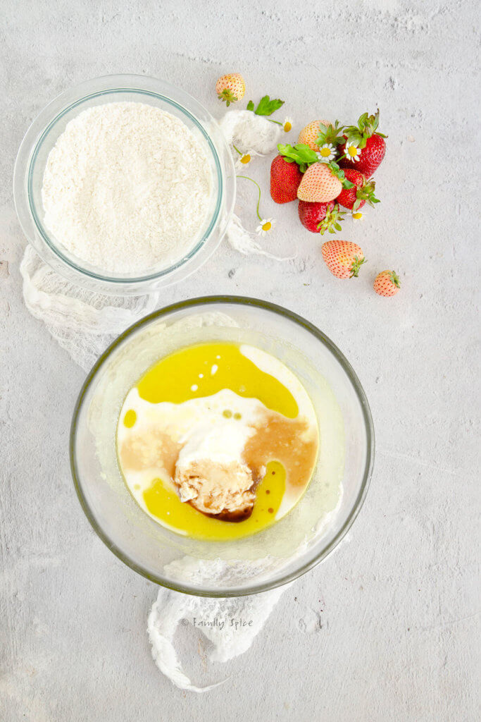 A glass mixing bowl with yogurt, milk and vanilla added to batter and another bowl with flour mixture in it