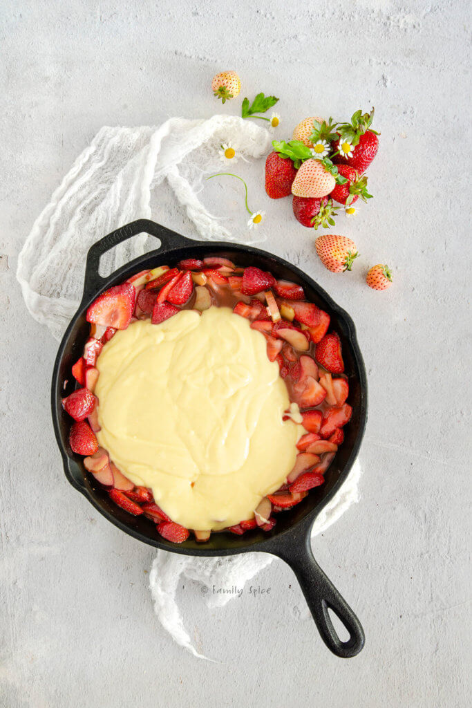 Pouring cake batter over strawberries and rhubarb in a cast iron skillet