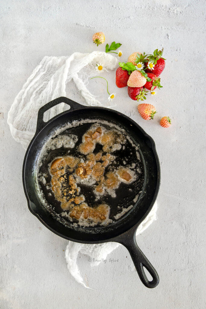 A cast iron skillet with melted butter and brown sugar in it and berries next to it