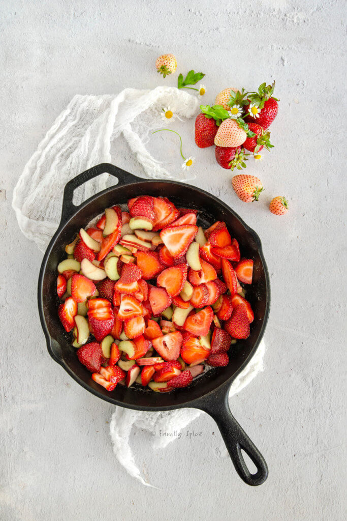 A cast iron skillet with chopped berries and rhubarb in it and berries next to it