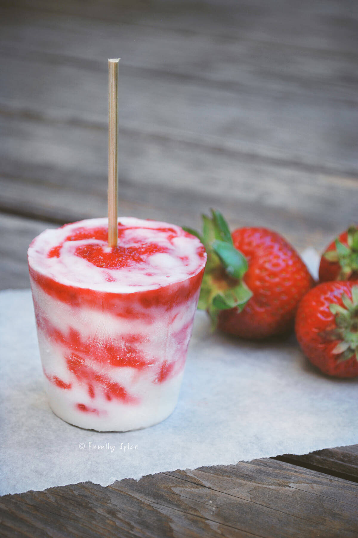 Homemade strawberry rhubarb creamsicle popsicles on a wood table with strawberries next to it