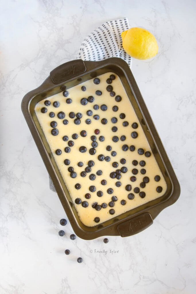 Lemon bar batter in a baking pan with blueberries scattered over it with a lemon next to it