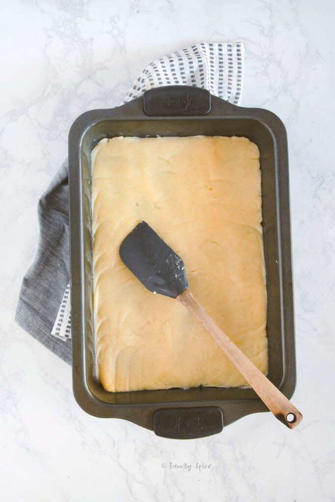 Shortbread dough pressed into a baking pan with a rubber spatula over it