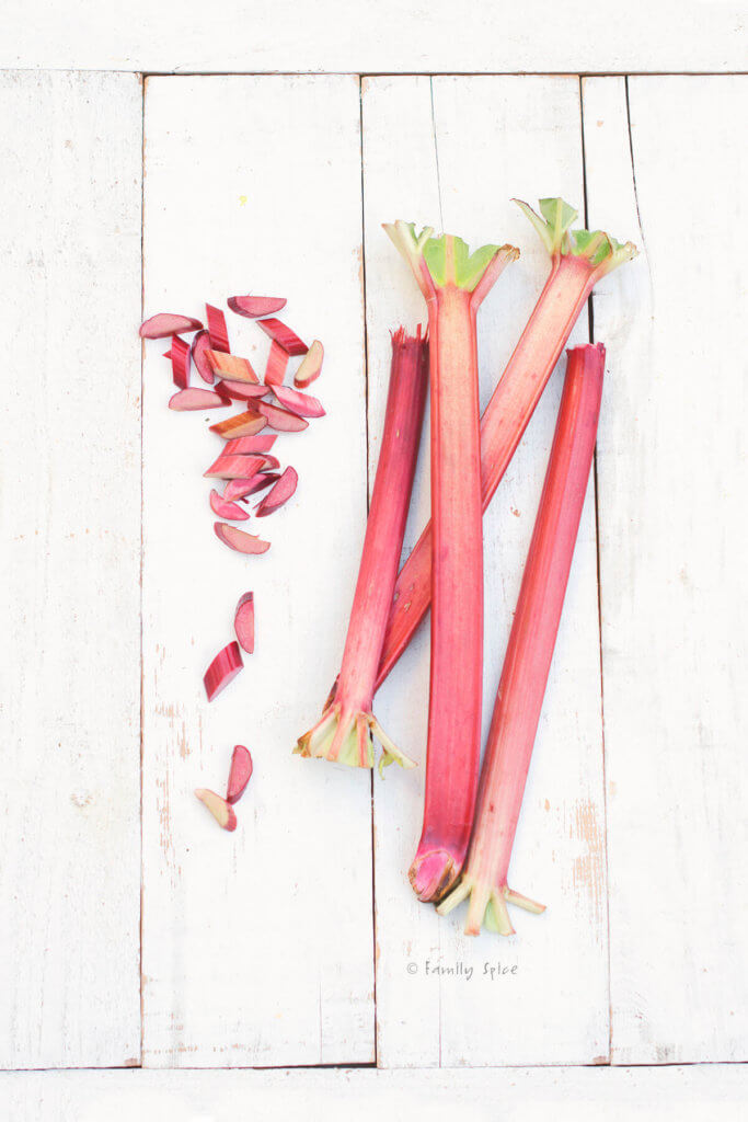 Fresh rhubarb stalks and slices on a white wood background