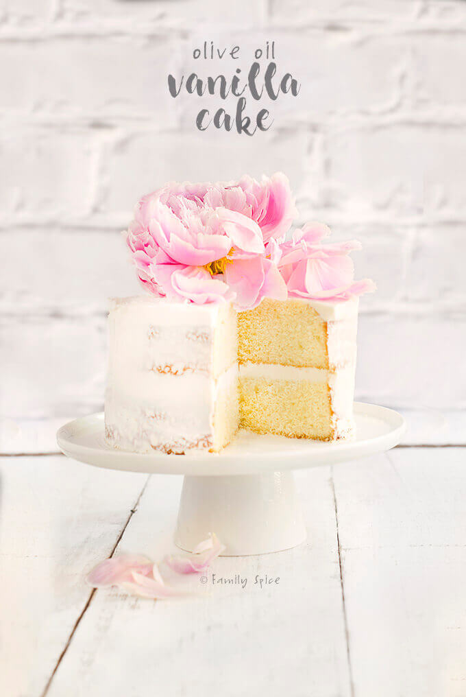 Easy olive oil vanilla cake cut open and frosted in white and topped with a pink flower by FamilySpice.com