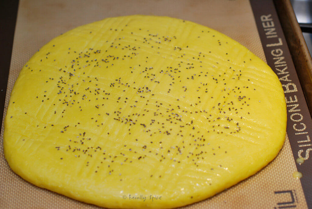 Flattened shirin chorek dough pressed with fork and topped with poppy seeds and ready to bake