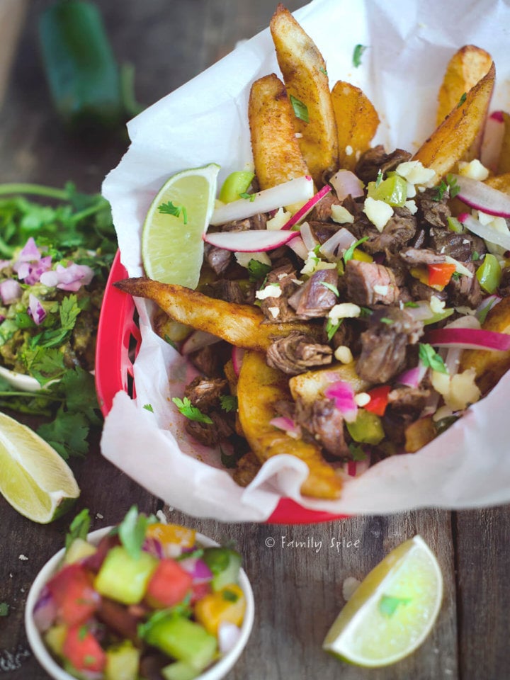 Closeup of a basket with loaded carne asada fries with ingredients around it
