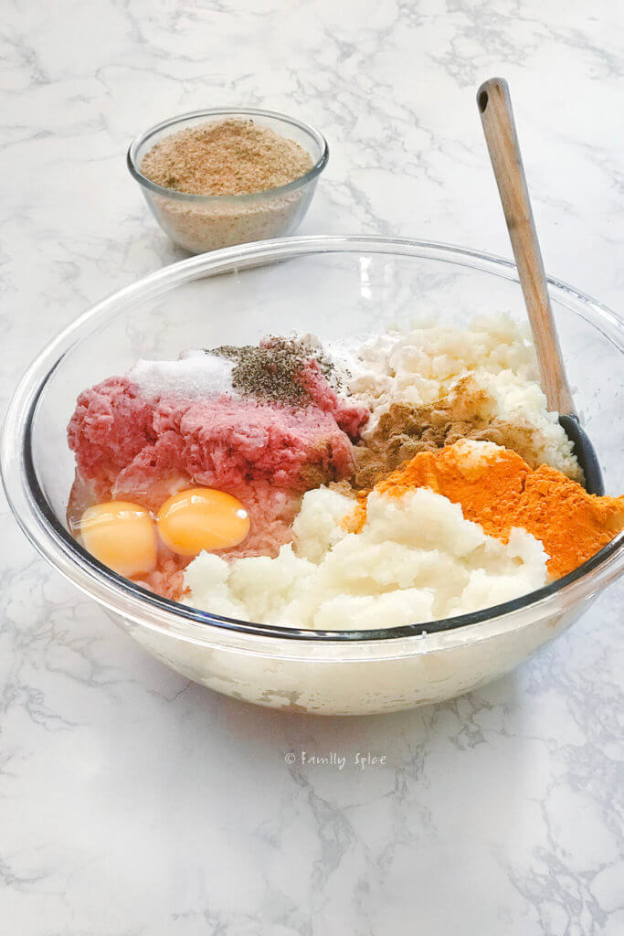 Closeup of a bowl with ingredients to make beef cutlet with a bowl of bread crumbs in the background