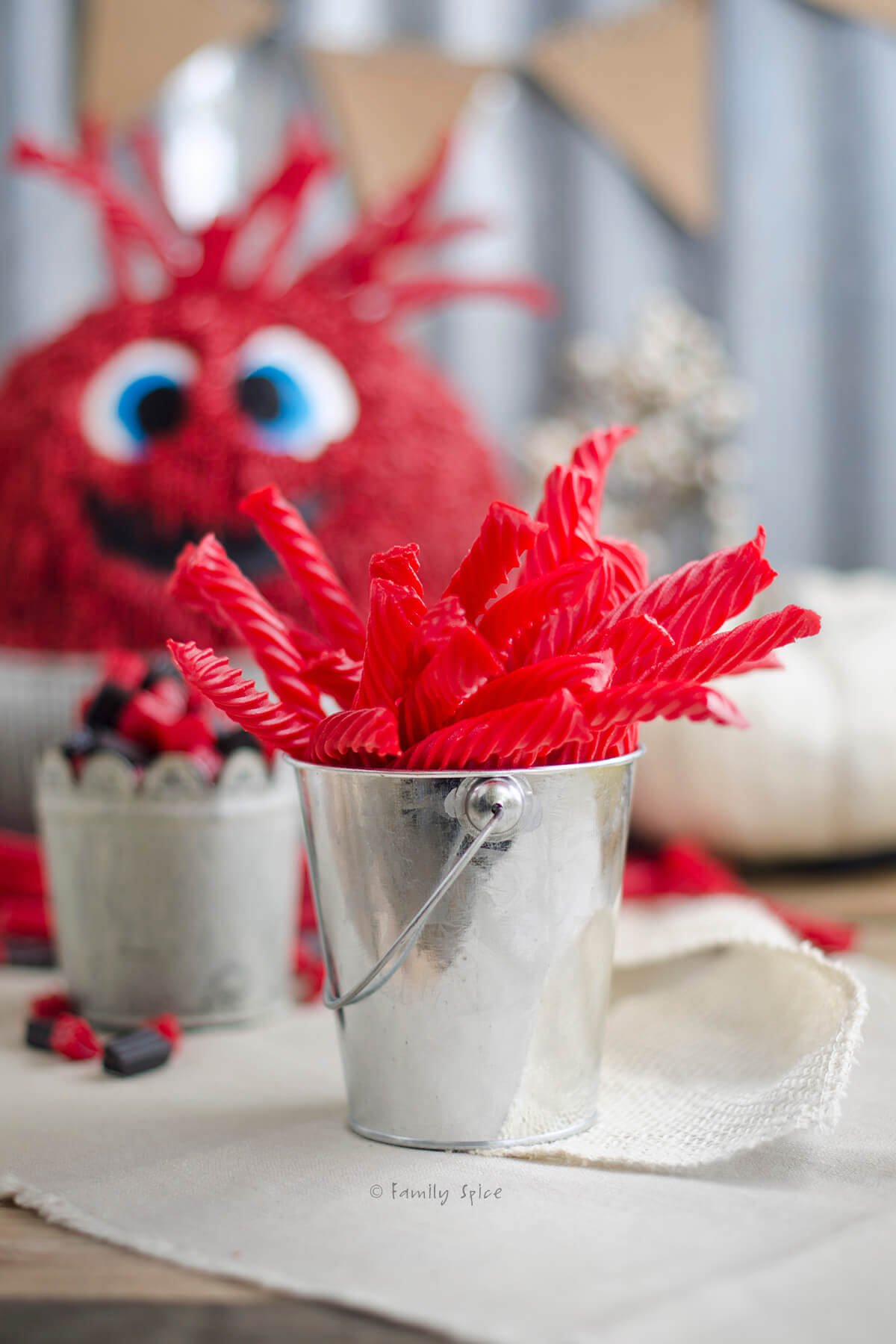 A metal cup with red red vine candies in it and monster cake behind it