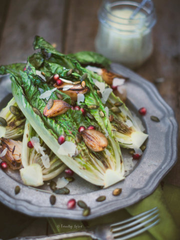 Closeup of a pewter plate with grilled romaine lettuce topped with roasted shallots and pomegranate arils