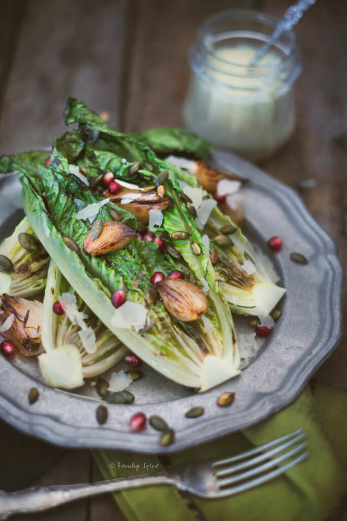 Closeup of a pewter plate with grilled romaine lettuce topped with roasted shallots and pomegranate arils