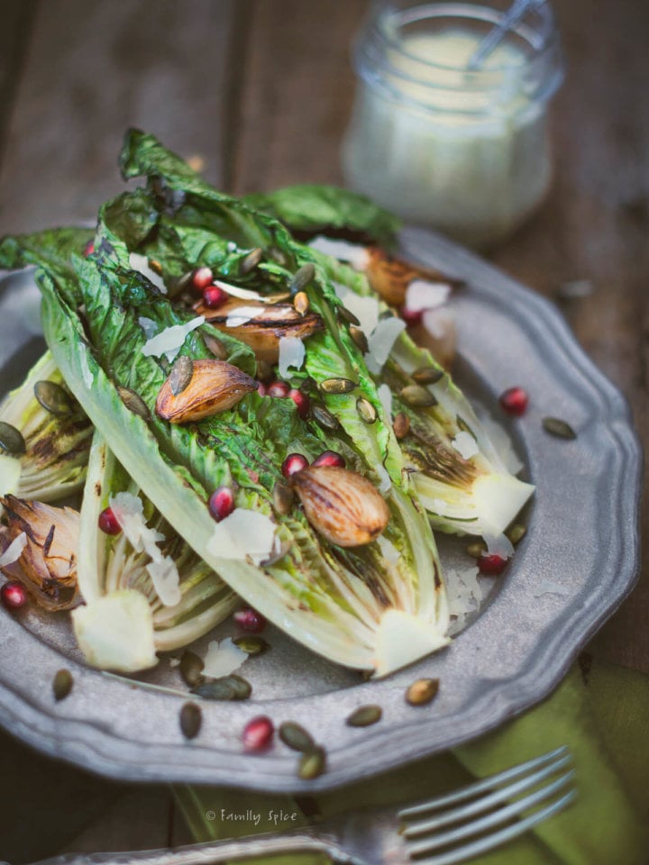 Closeup of a pewter plate with grilled romaine lettuce topped with roasted shallots and pomegranate arils
