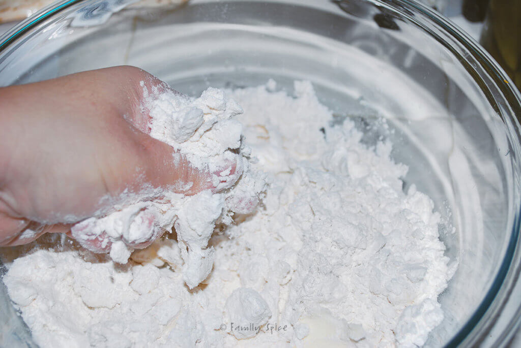 Hands squeezing butter in a flour mixture in a mixing bowl