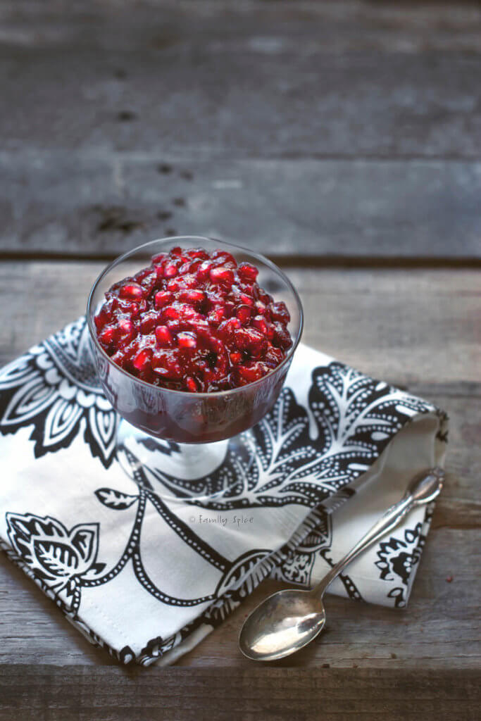 pomegranate cranberry sauce in a glass footed bowl on a dark wood background