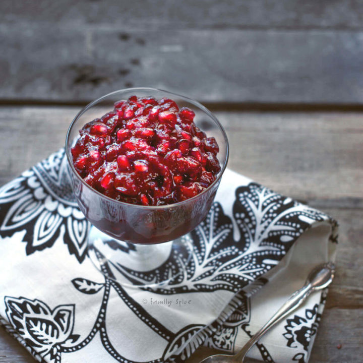 A glass footed bowl with cranberry pomegranate sauce on a rustic wood background