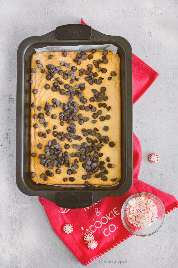 Shortbread cookie batter freshly baked in a 9x13 metal pan with chocolate chips sprinkled over it
