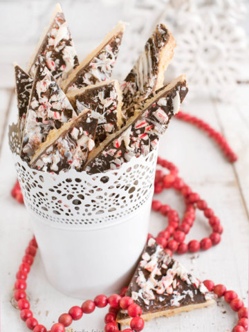 Several shortbread peppermint bark cookies in a white pail with a string of red beads around it