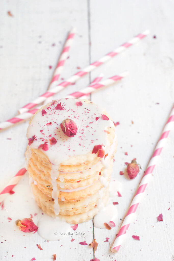 A stack of sugar cookies drizzles with white icing and dusted with dried rose petals with straws next to it