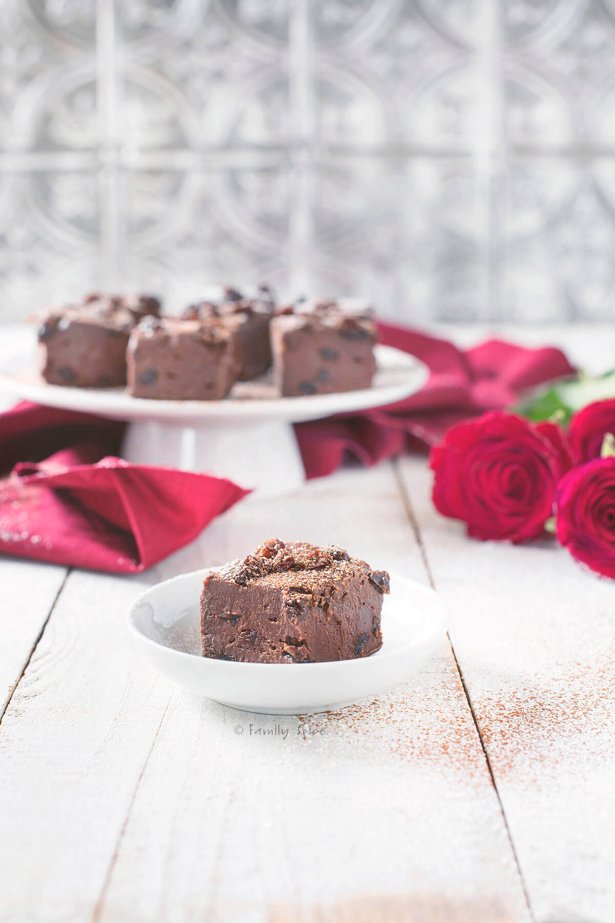 Closeup of Chocolate Rum Raisin Fudge on a White Cake Stand with Red Roses 